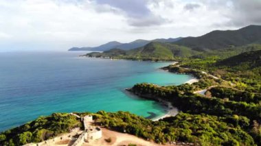 Yeşillikle kaplı tepeler. Tepenin tepesindeki antik yapıların kalıntıları. Ege kıyısı. Yol. Yunanistan