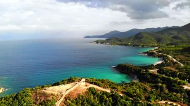 Yeşillikle kaplı tepeler. Tepenin tepesindeki antik yapıların kalıntıları. Ege kıyısı. Yol. Yunanistan