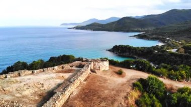 Tepenin tepesindeki antik yapıların kalıntıları. Yeşillikle kaplı tepeler. Ege kıyısı. Yol. Yunanistan