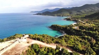 Yeşillikle kaplı tepeler. Tepenin tepesindeki antik yapıların kalıntıları. Ege kıyısı. Yol. Yunanistan