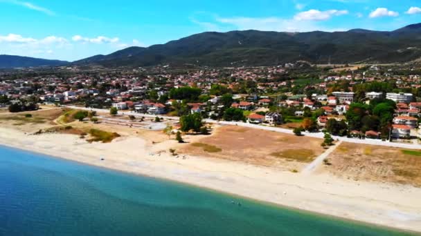 Panorama Asprovalty z wieloma budynkami i zielenią, zielone wzgórza na tle. Wybrzeże Morza Egejskiego. Plaża z parasolami i leżakami. Słoneczny dzień. Grecja — Wideo stockowe