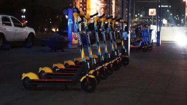 BUCHAREST, ROMANIA - 21 Kasım 2020: Geceleri paylaşmak için park halindeki elektrikli scooterlar, caddelerde hareket eden arabalar ve aydınlatma