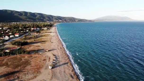 Vista da costa do mar Egeu em Asprovalta ao pôr do sol a partir do drone. Múltiplos edifícios e vegetação. Mar agreste, ondas com espuma. Grécia — Vídeo de Stock