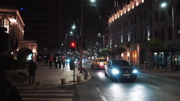 BUCHAREST, ROMÁNIA - NOVEMBER 21, 2020: Utcai táj éjjel egy út mozgó autókkal és ébresztő emberekkel, megvilágítás — Stock videók