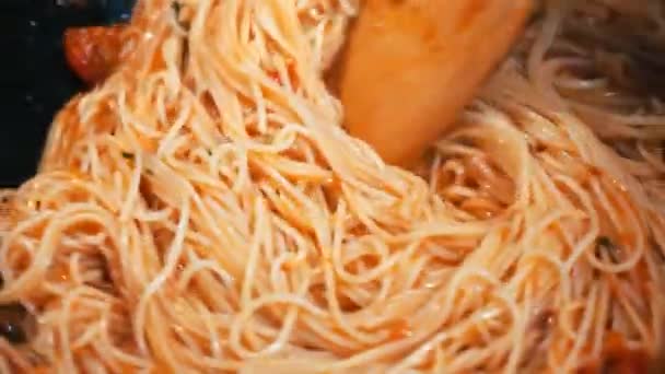 Un uomo sta mescolando spaghetti con salsiccia in una padella su un fornello — Video Stock