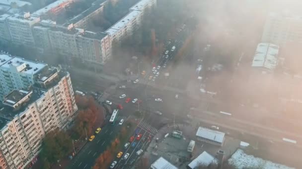 Hareket eden arabalarla kavşak, karşıdan karşıya geçen insanlar, çıplak ağaçlar ve konut binaları, yerden yükselen sis, Bükreş, Romanya 'daki bir insansız hava aracının manzarası — Stok video