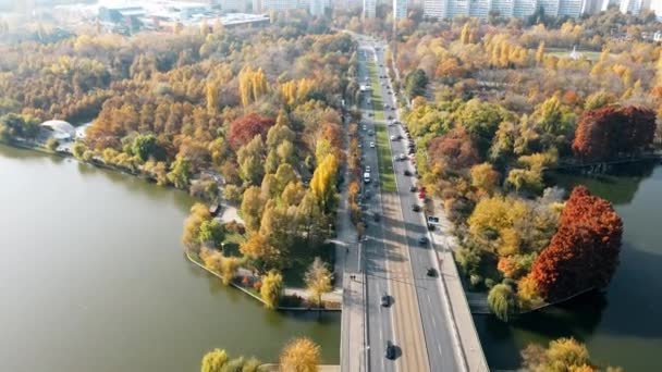 BUCHAREST, ROUMANIE - 18 OCTOBRE 2020 : Une route sur le lac avec des voitures en mouvement dans le parc Titan, de la verdure multiple et des bâtiments résidentiels. Vue depuis le drone — Video