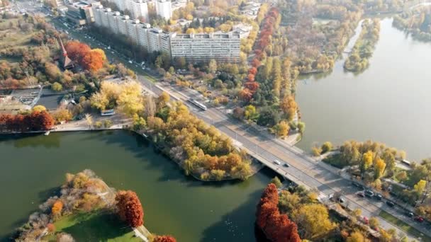 Une route sur le lac avec des voitures en mouvement dans le parc Titan, de la verdure multiple et des bâtiments résidentiels. Vue depuis le drone, Bucarest, Roumanie — Video