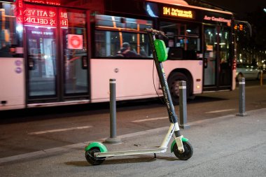 BUCHAREST, ROMANIA - 13 Kasım 2020: Arka planda otobüsle gece paylaşmak için park edilmiş elektrikli scooter