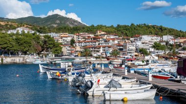 NEOS MARMARMARAS, GREECE - 8 Ekim 2020: Birden fazla demirlemiş yat ve teknesi olan Ege limanı, ahşap iskele, yeşil, açık hava koşulları olan bir tepenin üzerinde yer alan kasaba