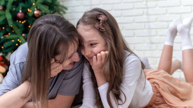 Anne ve kızı evdeki Noel ağacının yanında yerde gülümsüyorlar. Mutlu aile fikri