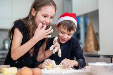 Kardeşler yemek pişiriyor ve mutfakta oynaşıyor, Noel şapkalı çocuk. Mutlu çocuk fikri