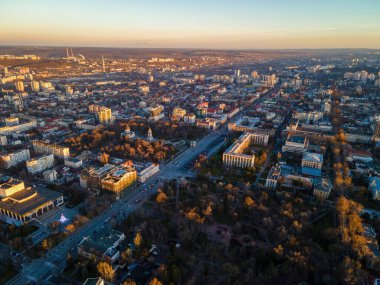 Chisinau 'nun günbatımında hava aracı görüntüsü. Birden fazla binanın panorama manzarası, hareket halindeki arabalı yollar, çıplak ağaçlar, merkez parklar. Moldova
