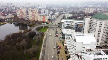 Chisinau 'nun hava aracı manzarası, birden fazla konut ve ticari binası olan cadde, hareket eden arabalı yol, çıplak ağaçlı göl.