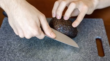 Avokado soyan bir adam yemek tahtasında bıçak kullanıyor.