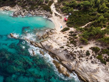 Mavi şeffaf su, çevresindeki yeşillikler, kayalar, çalılar ve ağaçlarla Ege kıyısı Yunanistan insansız hava aracının manzarası