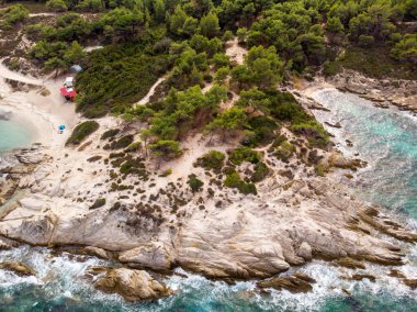 Mavi şeffaf su, çevresindeki yeşillikler, kayalar, çalılar ve ağaçlarla Ege kıyısı Yunanistan insansız hava aracının manzarası
