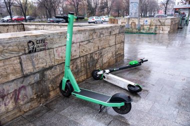 BUCHAREST, ROMANIA - 15 ARALIK 2020: Bir park etmiş Bolt ve Lime, hareket halindeki arabaları, yağmurlu ve bulutlu havalarda yol kenarında elektrikli scooterları düşürdü