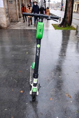 BUCHAREST, ROMANIA - 15 Aralık 2020: Islak ve bulutlu havada insanların hareket ettiği yolun yakınına park edilmiş elektrikli scooter