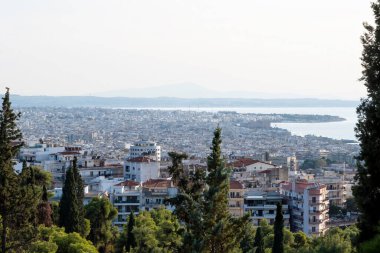 Yunanistan 'da bir tepeden Selanik Panoraması, birden fazla bina ve uzaktan Ege Denizi, ön planda yeşil ağaçlar
