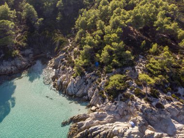 Mavi şeffaf suyla Ege kıyıları, etrafındaki yeşillikler, kayalar, çalılar ve ağaçlar, insansız hava aracı Yunanistan 'ın manzarası