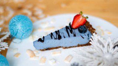 Çilekli, böğürtlenli ve kış süslemeli beyaz bir tabakta bir dilim kek. Yakın çekim.