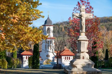 Gates of the Churchi Monastery. A lot of green buches and colored trees, stone cross in the center. Good weather in Moldova clipart