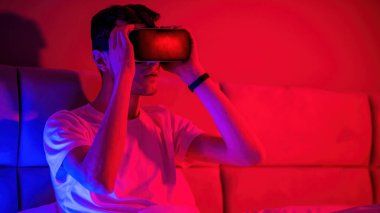 Yatakta mavi ve kırmızı ışıklı sanal gerçeklik gözlüklü genç adam etkilendi. Evde eğlence.