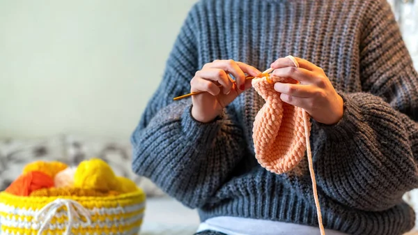 Woman in a sweater knitting on the bed using orange yarn