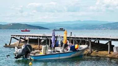 Ege kıyısı, tepeler ve Yunanistan 'ın Ouranoupolis kentindeki bir rıhtımda karaya vurmuş motorlu renkli bir tekne.