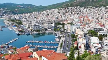 Kavala 'nın havadan görünüşü. İskan binaları, demirli yatları olan Ege limanı, insanların ve arabaların olduğu yollar, arka planda yeşil tepeler. Yunanistan