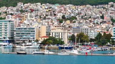 KAVALA, GREECE - 23 SEPTEMBER 2020: Ege kıyılarında liman ve demirlemiş yatları, arka planda yeşil tepeleri olan birden fazla bina
