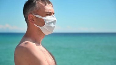 Yunanistan 'da Ege kıyılarında beyaz tıbbi maskeli bir adamın portresi, arka planda su.