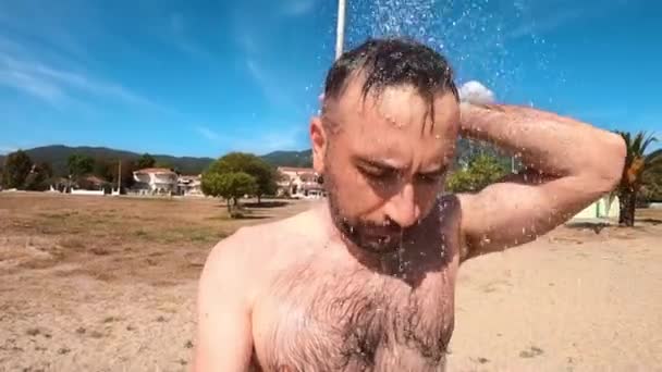 ギリシャの背景にある町アスプロバルタのビーチでシャワーを浴びている男 — ストック動画