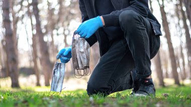 Tıbbi eldivenli bir adam parkta yerden kirli tıbbi maskeler alıyor. Kirlilik fikri