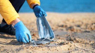 Tıbbi eldivenli bir adam gölün sahilinden kirli tıbbi maskeler alıyor. Kirlilik fikri