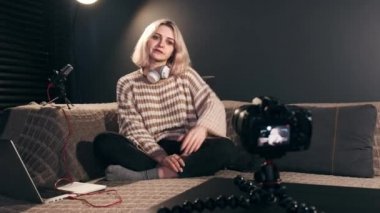 Genç içerik yaratan sarışın konuşan kız video kayıt yaparken üç ayaklı bir kamerayla kendini kameraya çekiyor. Evden çalışmak