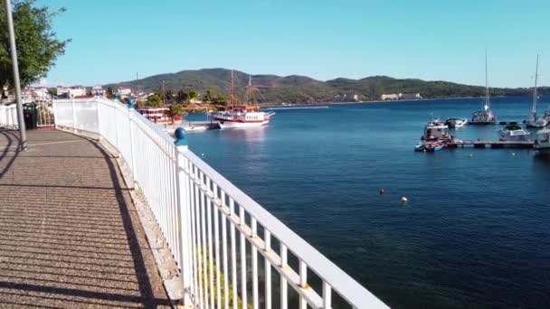 从有栅栏的人行横道上 可以看到一个宽阔的码头 停泊着帆船 青山和城镇 Neos Marmaras 慢动作 — 图库视频影像