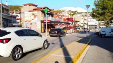 NEOS MARMARAS, GREECE - 8 Ekim 2020: Kafe, yeşillik, ikametgah binaları, hareket halindeki ve park halindeki arabaları olan şehir sokağı. Yavaş çekim