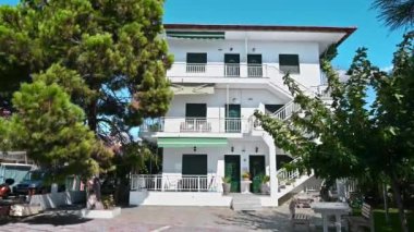 NIKITI, GREECE - 8 Ekim 2020: Üç katlı, teraslı ve merdivenli bir konut, etrafında birden fazla yeşillik, park halindeki arabalı bir yol