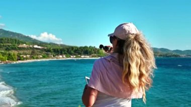 NEOS MARMARAS, GREECE - 8 Ekim 2020: Ege 'nin Ege kıyılarında telefonla fotoğraf çeken beyaz şapkalı ve güneş gözlüklü kadın