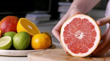 Ahşap bir tahtada kesilmiş bir greyfurt parçası gösteren bir kadın. Arka planda meyveler var. Yavaş çekim