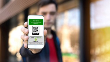 Akıllı telefonda Uluslararası Aşı Sertifikası COVID-19 QR kodu gösteren bir adam