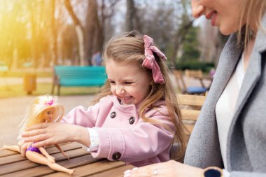 Mutlu anne ve kızı dışarıda oyuncak bebekle oynuyorlar.