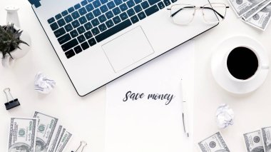 Finans işleriyle dolu bir masa. Laptop, para, kahve, kalem, kağıt