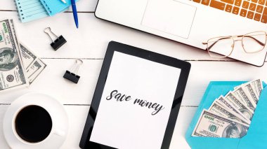 Finans işleriyle dolu bir masa. Laptop, kahve, para, tablet, kalem, kağıt