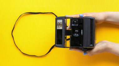 Sarı arka planda klasik fotoğraf makinesi tutan kadın eller.