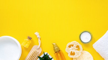 Kişisel bakım şeylerinin bileşimi. Sarı arka planda süngerler, fırçalar, kremler, şişeler ve mumlar