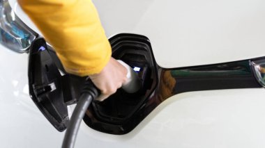 Şarj aletini beyaz bir elektrikli arabaya takan adam.