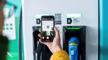 CHISINAU, MOLDOVA - 26 Nisan 2021: Bir adam akıllı telefonuyla elektro arabanın şarj cihazında qr kodunu tarıyor